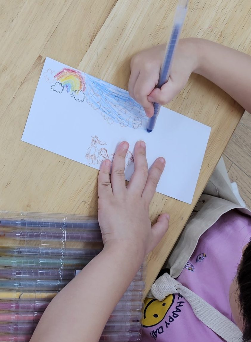 전사용 종이에 색연필로 무지개와 하늘을 그리는 아이 손