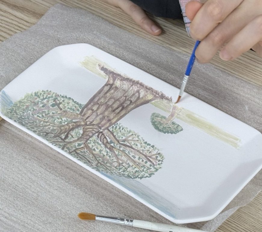 긴 네모 접시에 붓으로 나무를 칠하고 있는 손