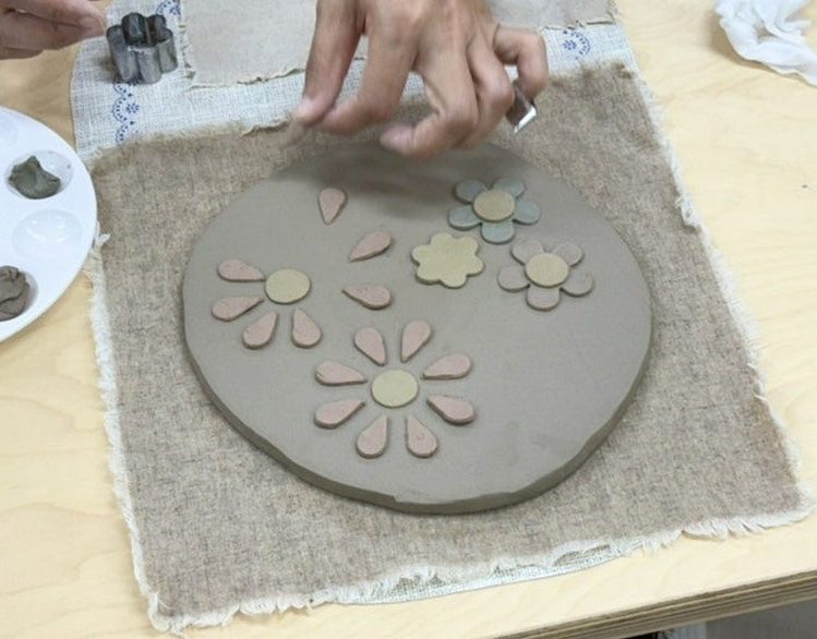 모양틀과 팔레트 옆에서 바탕 흙 위에 꽃 조각을 놓는 손